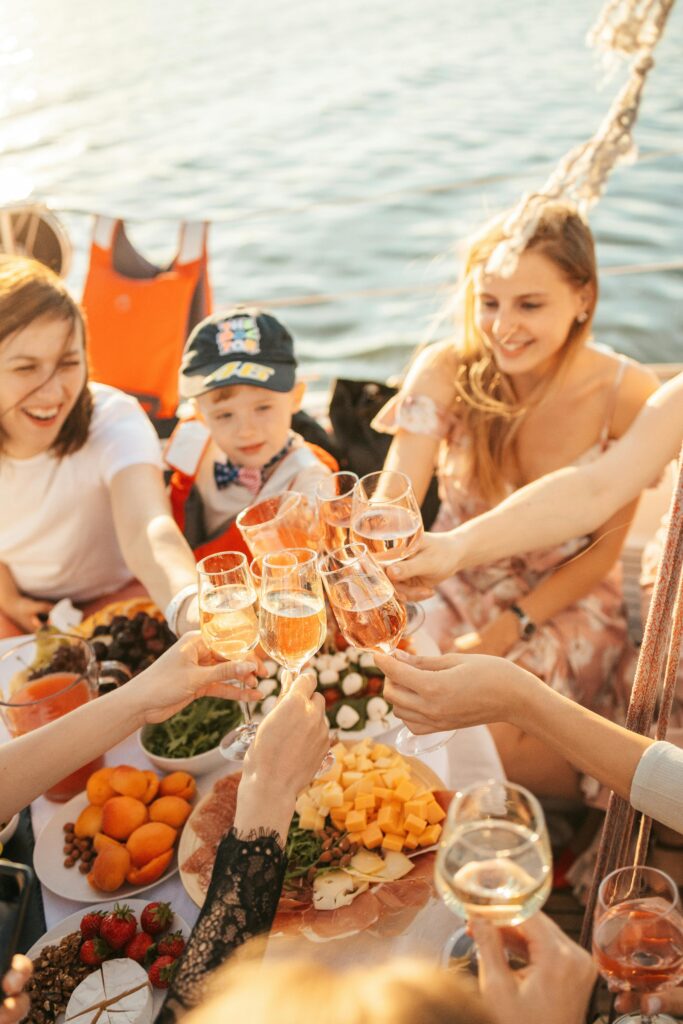 Group of friends enjoying a summer yacht party with drinks and a vibrant food spread.